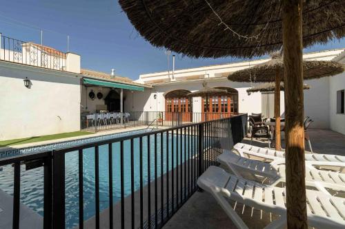 a swimming pool with white chairs and an umbrella at Casa Rural "compartida" La Loma Granero in Granada