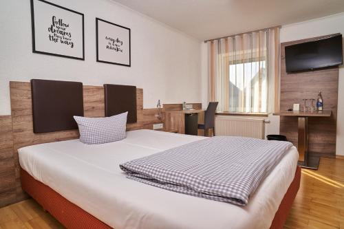 a bedroom with a bed with a television and a desk at Hotel Römer by Fairway Hotels in Günzburg