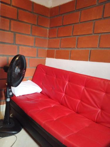 a red couch with a fan next to a brick wall at Mi pueblo natal Aptos y habitaciones in Necoclí