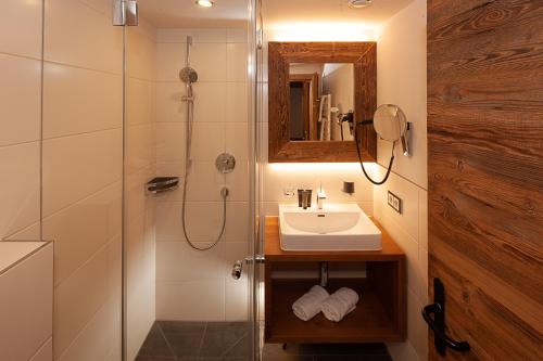 a bathroom with a sink and a shower with a mirror at Das alpine Lifestyle Berghotel Madlener in Damuls