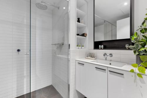 a white bathroom with a shower and a sink at Elegant Inner-West 2-Bed with City Views & Pool in Melbourne