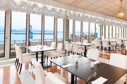 a restaurant with tables and white chairs and windows at Hotel Den Haag Huis Ten Bosch in Sasebo