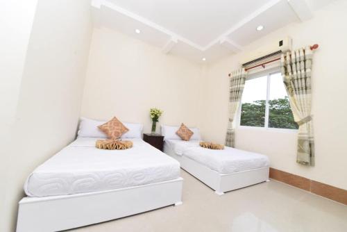 2 Betten in einem weißen Zimmer mit Fenster in der Unterkunft Khách sạn Đồng Tháp - Hoàng Gia Minh Lợi in Mỹ An