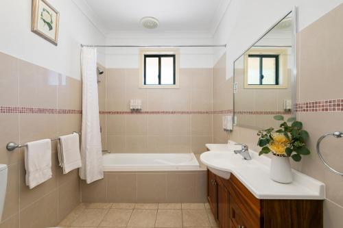 uma casa de banho com uma banheira, um lavatório e um espelho. em Potters Apartments em Cessnock