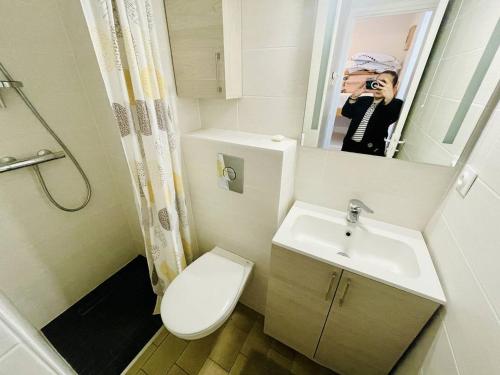 une femme prenant une photo d'une salle de bains avec toilettes et lavabo dans l'établissement Beau studio proche plage avec parking et wifi - FR-1-723-141, au Cap d'Agde