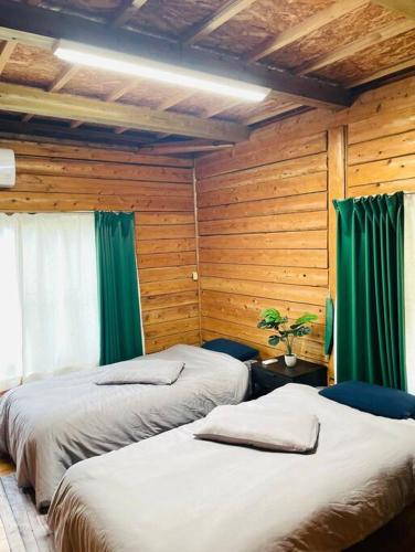 two beds in a room with wooden walls and green curtains at Wood retreatみやざき in Miyazaki