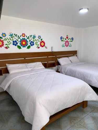 dwa łóżka w pokoju z kwiatami na ścianie w obiekcie PERLASCHALLAY w mieście Ayacucho