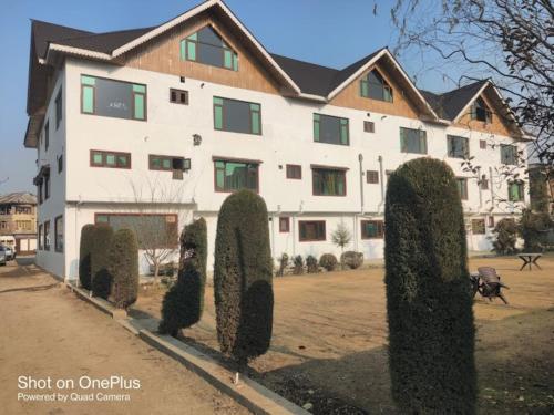 un gran edificio blanco con arbustos delante en Hotel Taj Residency Srinagar en Srinagar