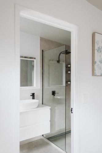 a white bathroom with a sink and a mirror at Wallaby House at On Burgum Pond in Maleny