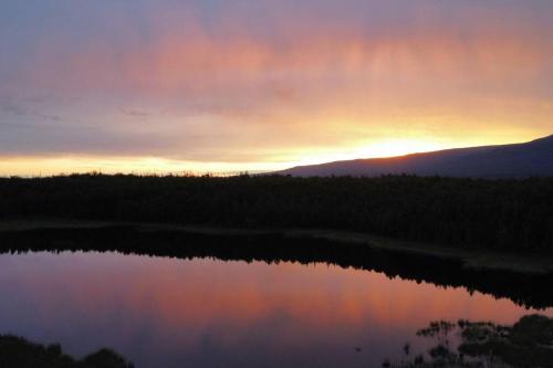 a sunset over a body of water with trees at Hatcher Pass Lakeside Hideaway with Hot Tub! in Wasilla