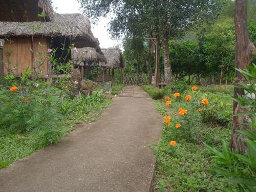 een pad in een tuin met bloemen en een rieten hut bij Maila 