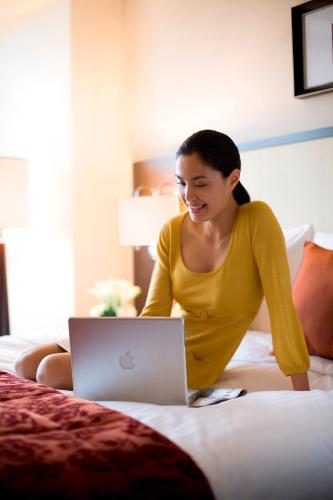 a woman sitting on a bed with a laptop at Courtyard By Marriott Shanghai Xujiahui in Shanghai