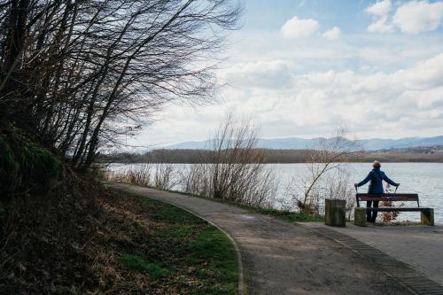 a woman sitting on a bench next to a lake at Apartament ACTIV jezioro góry in Żywiec