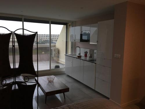 une cuisine avec des placards blancs et une grande fenêtre dans l'établissement Village Naturiste Le Cap d’Agde Heliopolis Sud Vue Mer, au Cap d'Agde