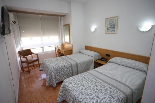 a room with two beds and a chair and a window at Hotel Cervantes in Alicante
