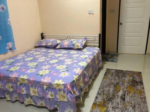 ein Schlafzimmer mit einem Bett mit einer lila Bettdecke und einem Teppich in der Unterkunft HOMESTAY PERLIS MURAH in Arau