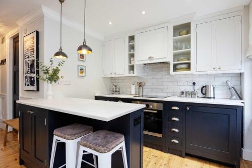 a kitchen with white cabinets and a blue island with stools at Veeve - Bloomsbury Culture in London