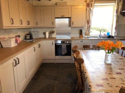 a kitchen with white cabinets and a table with flowers on it at Brynonnen Llangrannog in Llanllwchaiarn
