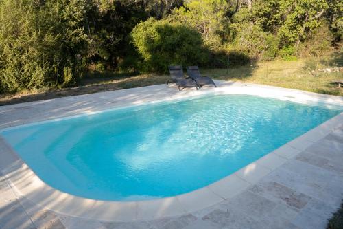 uma piscina com duas cadeiras sentadas ao lado em Chalet dans plusieurs hectares de nature em Barjols