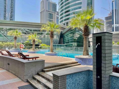 a pool with chairs and palm trees in a city at Rustic Elegance By The Lake Studio Cabin In Jlt in Dubai
