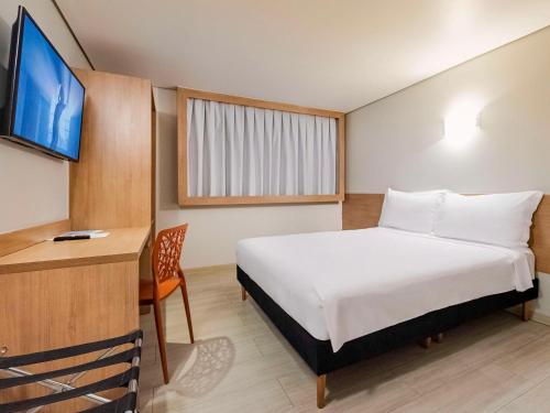 Schlafzimmer mit einem Bett, einem Schreibtisch und einem TV in der Unterkunft ibis Styles Goiânia Shopping Estação in Goiânia