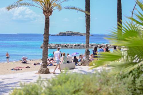 people on a beach with palm trees and the ocean at Hotel Figueretes in Ibiza Town