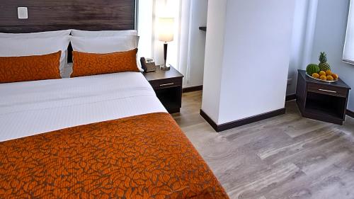 a bedroom with a bed with an orange bedspread and two tables at AZ Hotel in Bogotá