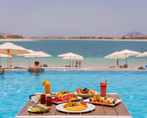 ein Tisch mit Tellern voller Essen neben einem Swimmingpool in der Unterkunft C Central Hotel and Resort The Palm in Dubai