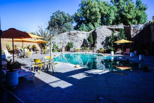 a pool with chairs and umbrellas and a table and chairs at Hotel La Perle du Sud in Ouarzazate