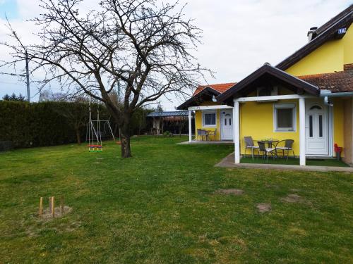 a yard with a yellow house and a tree at Soba Milica in Palić