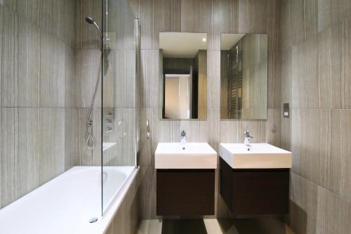 a bathroom with two sinks and a shower and a tub at Barons Court Queens Club by Viridian Apartments in London