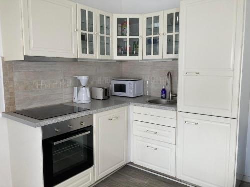 a white kitchen with white cabinets and a microwave at La petite maison bleue in Gruissan