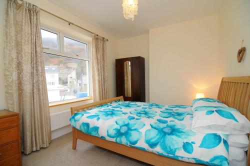 1 dormitorio con 1 cama con edredón de flores azul y ventana en Gerlan Llangrannog, en Llangranog