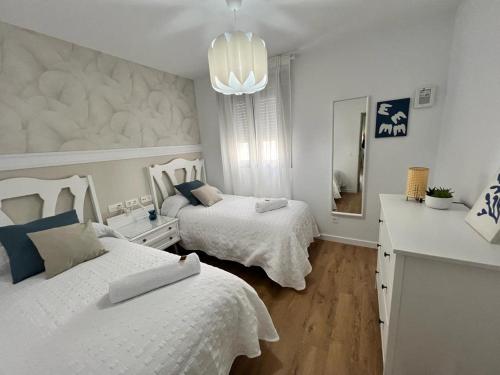 Habitación blanca con 2 camas y lámpara de araña. en Jardines del Porvenir 2 en Puerto Real