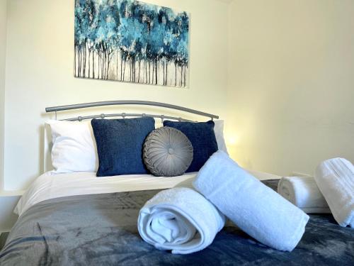 a bed with blue pillows and a painting on the wall at New Executive Apartment Perfect for Contractors & Pilots in Bishops Stortford