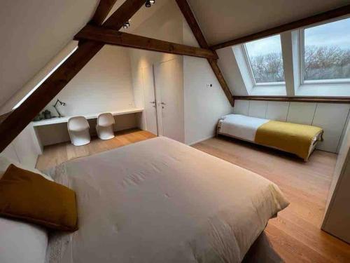 a attic bedroom with a large bed and two windows at Gezellig huis met open haard en fenomenale tuin in Koksijde