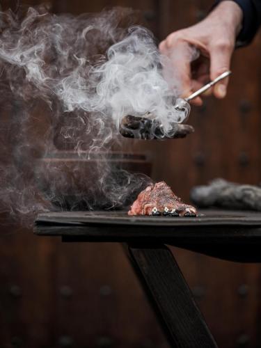 a person cooking meat on a grill with smoke at Botanic Sanctuary Antwerp - The Leading Hotels of the World in Antwerp