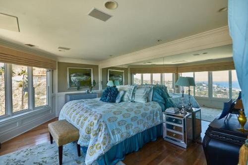 a bedroom with a bed with a blue bedspread and windows at UNEQUALLED LUXURY VILLA BEACH 7000ft 180 VIEW in Laguna Beach