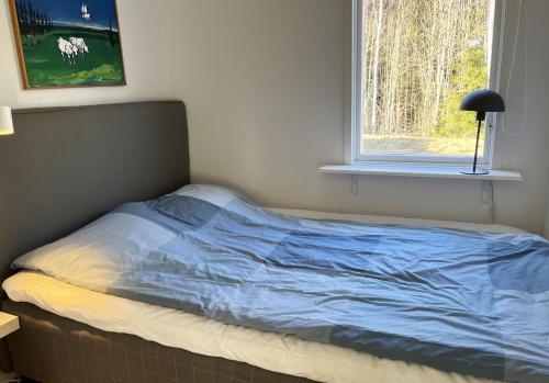 a bed with a blue comforter sitting next to a window at Nice cottage located by the lake Nommen in Björköby