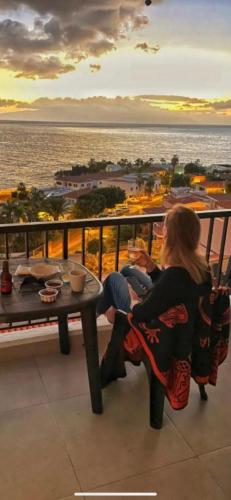 a woman sitting at a table on a balcony overlooking the ocean at Sunset Seaview La Arena in Puerto de Santiago
