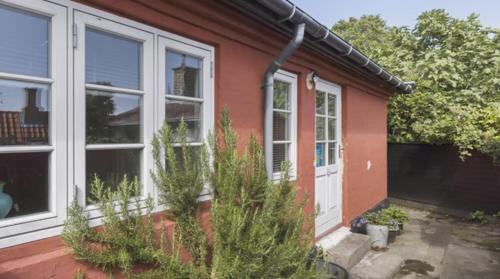 una casa roja con una puerta blanca y algunas plantas en Rummeligt byhus i Allinge med værelse i stueplan og havkig, en Allinge