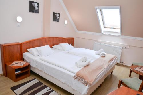 a bedroom with a bed with white sheets and a window at Major Panzió és Étterem in Hajdúszoboszló