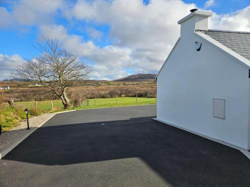 a white building with a driveway next to a road at Cosy 1 bedroom cottage, Ideal quiet getaway. in Creeslough