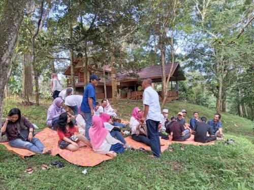 a group of people sitting on the grass in front of a house at Joben Evergreen Camp in Tetebatu