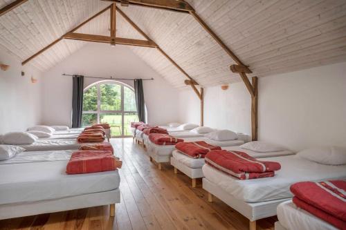 Habitación con una fila de camas blancas con almohadas rojas. en Gîte les Arcades 25 couchages, en Saint-Gildas-des-Bois