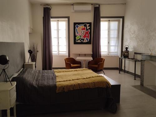 a bedroom with a bed and a table and two windows at LE PATIO in Grignan