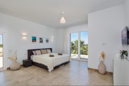 a white bedroom with a bed and a large window at Villa Es Trenc in Campos