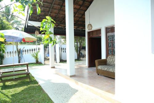a porch of a house with a bench and an umbrella at Coco Mango Hostel in Hiriketiya