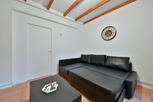 - un canapé en cuir noir dans le salon avec une horloge dans l'établissement Cozy appartment near Stade de France, à Saint-Denis