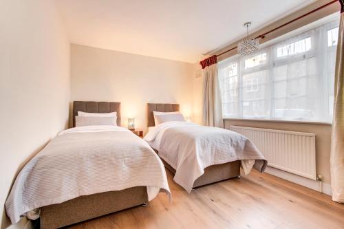2 camas en un dormitorio con ventana en Bright Charming Apartment In Ealing, en Londres